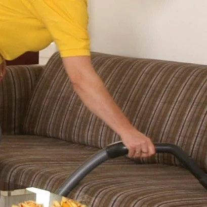 Eine Person saugt ein gestreiftes Sofa mit einem Staubsauger ab.